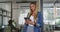 Caucasian businesswoman leaning in doorway using tablet, smiling to camera in busy office