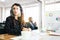 Caucasian businesswoman wearing face shield, sitting at meeting table with notebook, pen and tablet with blur African businessman