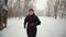 caucasian candid Woman in black jacket and hat runs through park in winter doing daily cardio workout. Woman runs