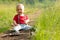 Caucasian, cheerful child sitting on the ground. Green grass and forest around.