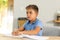 Caucasian cute blind boy reading braille book on table while sitting at home, copy space