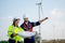 Caucasian engineer man and woman discuss together using drawing paper and stay in front of row of windmill or wind turbine with