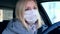 Caucasian european woman driving a car and wearing white surgical medical face mask as a way of protection against coronavirus and