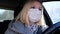 Caucasian european woman driving a car and wearing white surgical medical face mask as a way of protection against coronavirus and