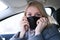 Caucasian european woman sitting in a car and wearing black surgical medical face mask as a way of protection against coronavirus