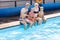 Caucasian family having fun by their swimming pool. Happy young family splashing water with hands and legs while sitting