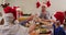 Caucasian family in santa hats toasting and enjoying lunch together while sitting on dining table at