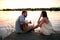 Caucasian female enjoying in company of a beardy male playing guitar by the lake at sunset