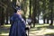 Caucasian Female Poses in Maleficent Clothing and Horns in Spring Forest. Holding Crook with Mirror Ball