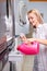 caucasian female pours a greasy detergent from pink bottle into the washing machine compartment