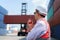 Caucasian foreman man is using walkie talkie to command his workers with crane lifting container in background in container depot