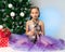 Caucasian girl 9 years old in purple dress holding playful Sphynx Cat sitting near Christmas tree