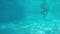 Caucasian girl in blue bikini walks in front of camera lens in blue pool. View from underwater