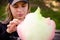 Caucasian girl in cap tears off pieces and eats candy-floss. Texture of multicolored candy-floss. Happy teenage girl enjoys sweets