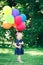 Caucasian girl child in blue dress with colorful balloons, in field meadow park