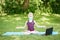 Caucasian girl child in face mask doing sport workout outdoor online. Video yoga on Internet. Kid learning training on backyard at