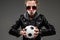Caucasian girl with rough facial features in a black jacket holds soccer ball isolated on black background