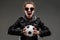 Caucasian girl with rough facial features in a black jacket holds soccer ball isolated on black background