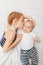 Caucasian girl sister holding kissing little baby, lying on bed