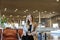 Caucasian girl sitting in airport hall with tablet near valise and wearing grey coat.