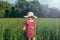 Caucasian girl in straw hat and red pink rustic dress walking in tall high grass in meadow outdoor