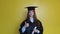 Caucasian girl student shows finger up while staying in front of camera with graduating diploma in her hands