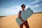 Caucasian girl in sunglasses ready to go sandsurfing. SHe holds surf in her hands and smile.