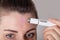 Caucasian girl treats acne on her face in the forehead area with a laser cosmetic pen on her face, macro