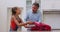 Caucasian grandfather in kitchen preparing packed lunch talking with granddaughter giving lollipop