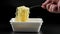 caucasian hand with fork stirring cooked instant noodles from styrofoam container on black background in slo-mo