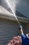 A caucasian hand with a latex glove arm holding a water sprayer wand power washing the gutters and roof of a house