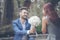 Caucasian handsome man giving flowers to asian girlfriend asking for proposing to marry him at green park. Couple lover on