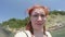 Caucasian happy funny red-haired girl looks into camera lens against background of sea and sandy steep green beach