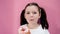 Caucasian healthy preschool kid with ponytails eats donut, enjoys and smiles. Childhood organic concept. Pink background