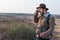 Caucasian hiker man with a beard, wearing a brown jacket, backpack, taking a picture of the field