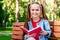 Caucasian Kid Girl Sitting In The Bench While Reading Book in the Park, Education concept. Great Resting Activitie on