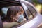 Caucasian little girl  wearing mask looking out of the open window of a car.