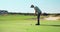 Caucasian male golfer wearing cap and golf clothes, swinging and hitting ball into hole, playing at green lawn