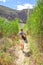 Caucasian male hiking through Montagu Springs valley and Mountain range with large red rocky outcrops and lush green vegetation