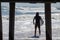 A caucasian male in a wetsuit holding a surfboard is seen standing by at the shoreline before entering the rough ocean