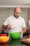 Caucasian man, between 30-39 years old, with cup in hand adding ingredients in a bowl, to prepare a cake