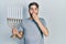 Caucasian man with beard holding menorah hanukkah jewish candle covering mouth with hand, shocked and afraid for mistake