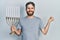 Caucasian man with beard holding menorah hanukkah jewish candle screaming proud, celebrating victory and success very excited with