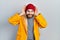 Caucasian man with beard wearing yellow raincoat smiling pulling ears with fingers, funny gesture