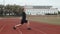 Caucasian man in black shorts and a T-shirt stretches his legs and back at the stadium before running, side view