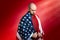 A Caucasian man covered with an American flag stands in a humble and proud pose. Red background. Copy space. Concept of memorial