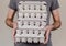 Caucasian man with gray t-shirt holding four cardboard egg boxes full of chicken eggs