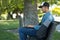 Caucasian man listening to music with wireless earbuds and his laptop on a park bench