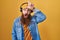 Caucasian man with long beard listening to music using headphones making fun of people with fingers on forehead doing loser