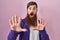 Caucasian man with long beard standing over pink background afraid and terrified with fear expression stop gesture with hands,